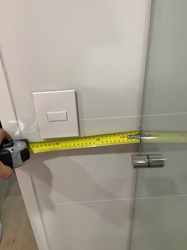 Image of tape measure showing distance between a light switch and a shower entry